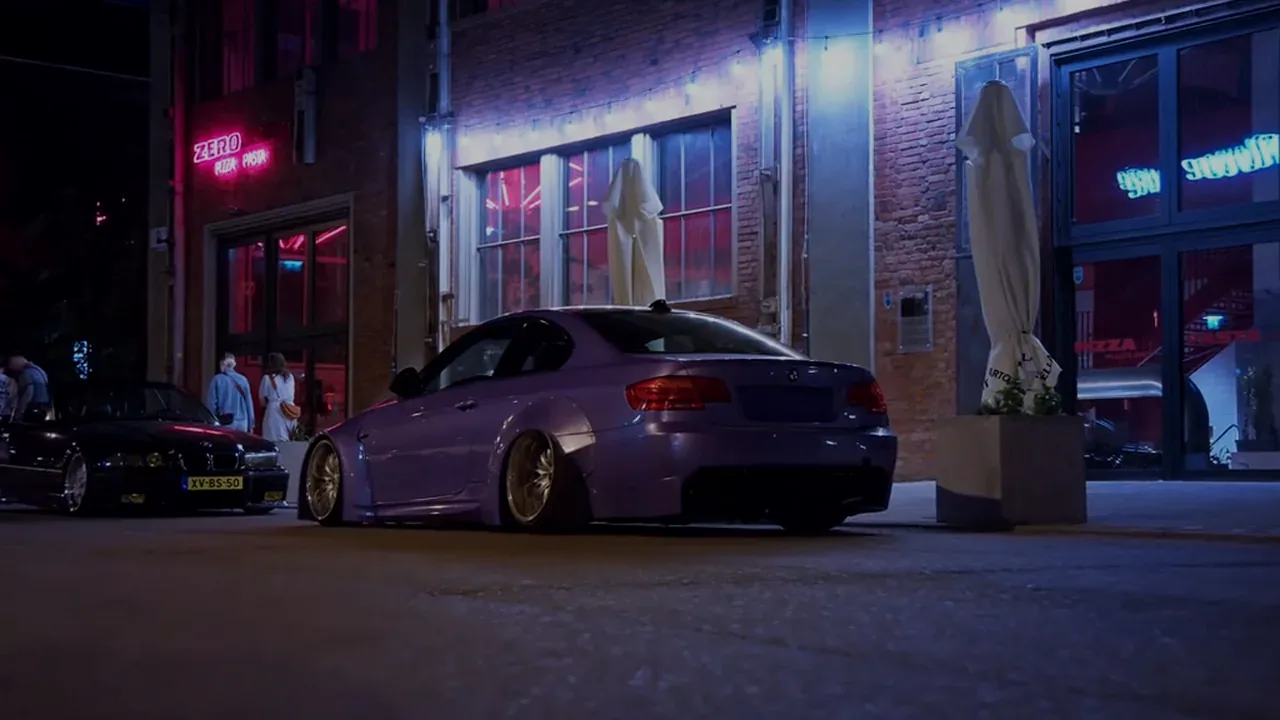 Widebody purple coupe parked at night outside a brick cafe, neon reflecting on the paint.
